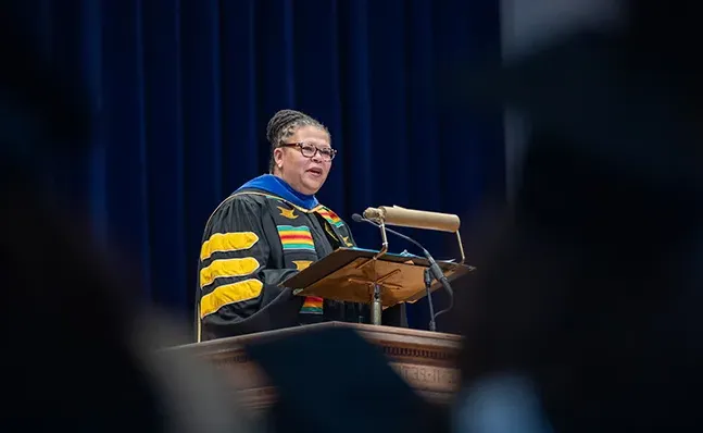 Sarah Willie-LeBreton in academic regalia, speaking at the School for Social Work commencement ceremony.