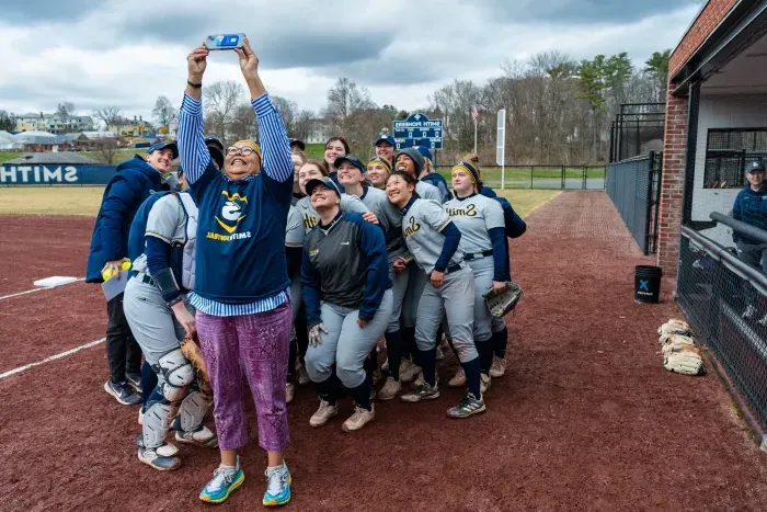 Sarah Willie-LeBreton takes a selfie with the softball team behind her.